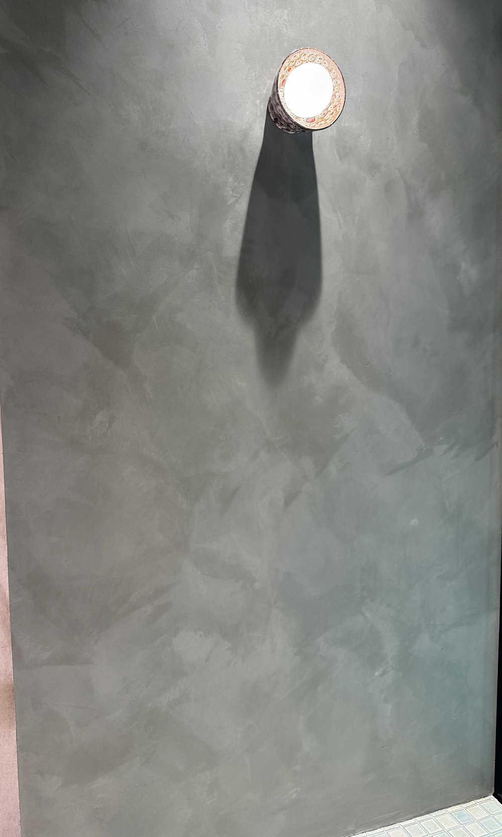 Sage green Venetian plaster wall with sconce shadow